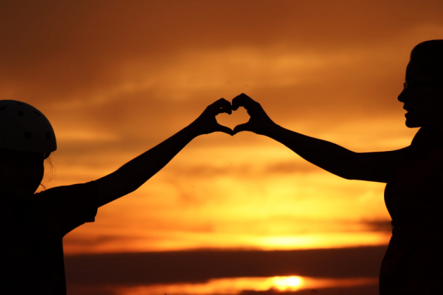 Stock photo of people making a heart shape with their hands in front of a sunset