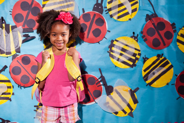 Young girl with backpack in front of a school mural with ladybugs.