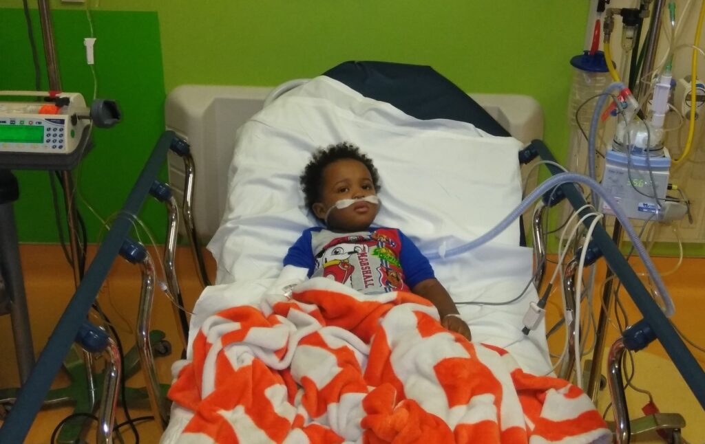 Young boy on a hospital bed attached to several medical tubes