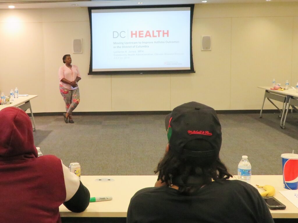 Person giving a presentation. Projected screen says DC Health.