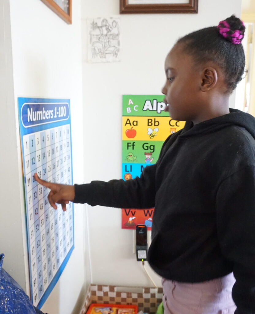A child counting numbers on a chart pasted to the wall