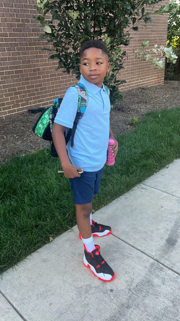 Kamari on the sidewalk heading to school, looking over his shoulder with backpack on.