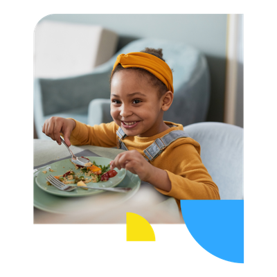 Smiling child seated at a table eats food