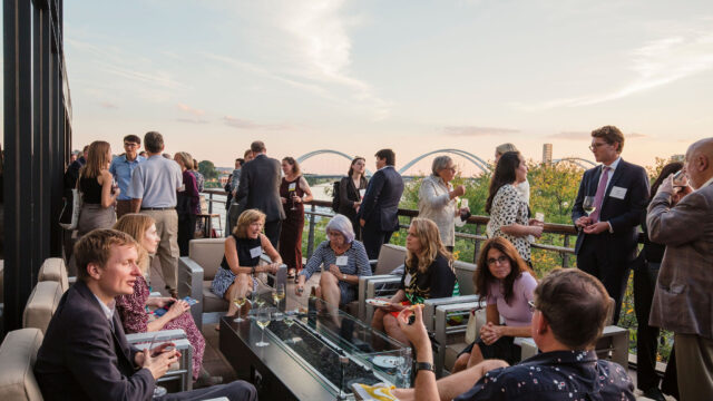 A group of people sitting on the outside terrace of District Winery with the Anacostia Bridge in the background during sunset.