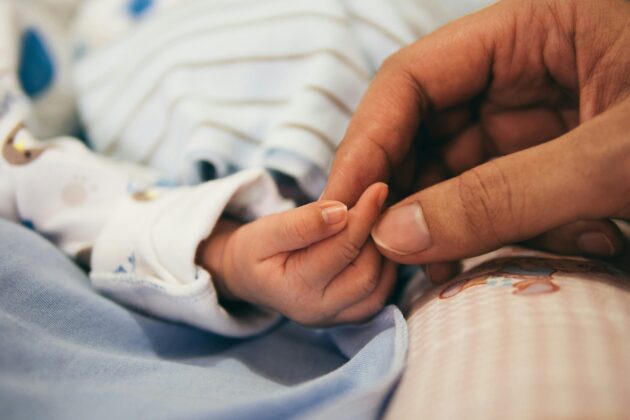 Close up of an adult's hand lightly holding an infant's hand, touching at the fingertips.