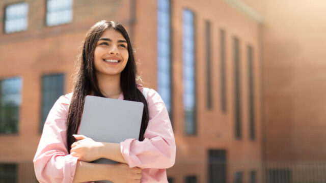 Young woman holding laptop in front of school building