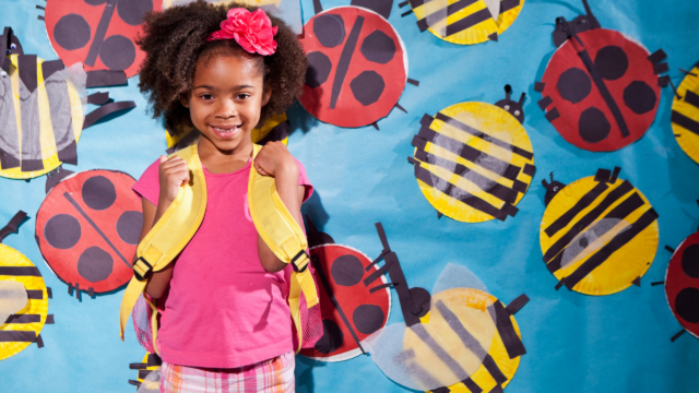 Young girl with backpack in front of a school mural with ladybugs.